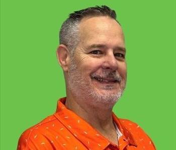 Man in orange shirt in front of green background.